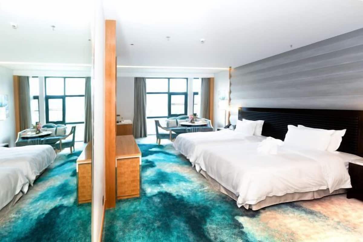 Quarto de hotel com uma cama grande, uma mesa e uma cadeira. Há uma janela com cortinas, e o quarto tem um design moderno.