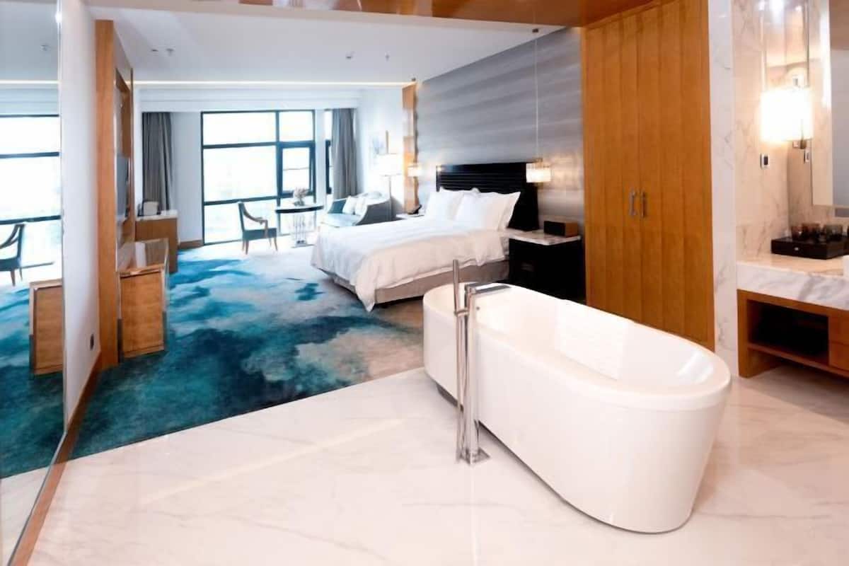 Quarto de hotel moderno com uma cama grande, uma banheira e vista para a cidade.