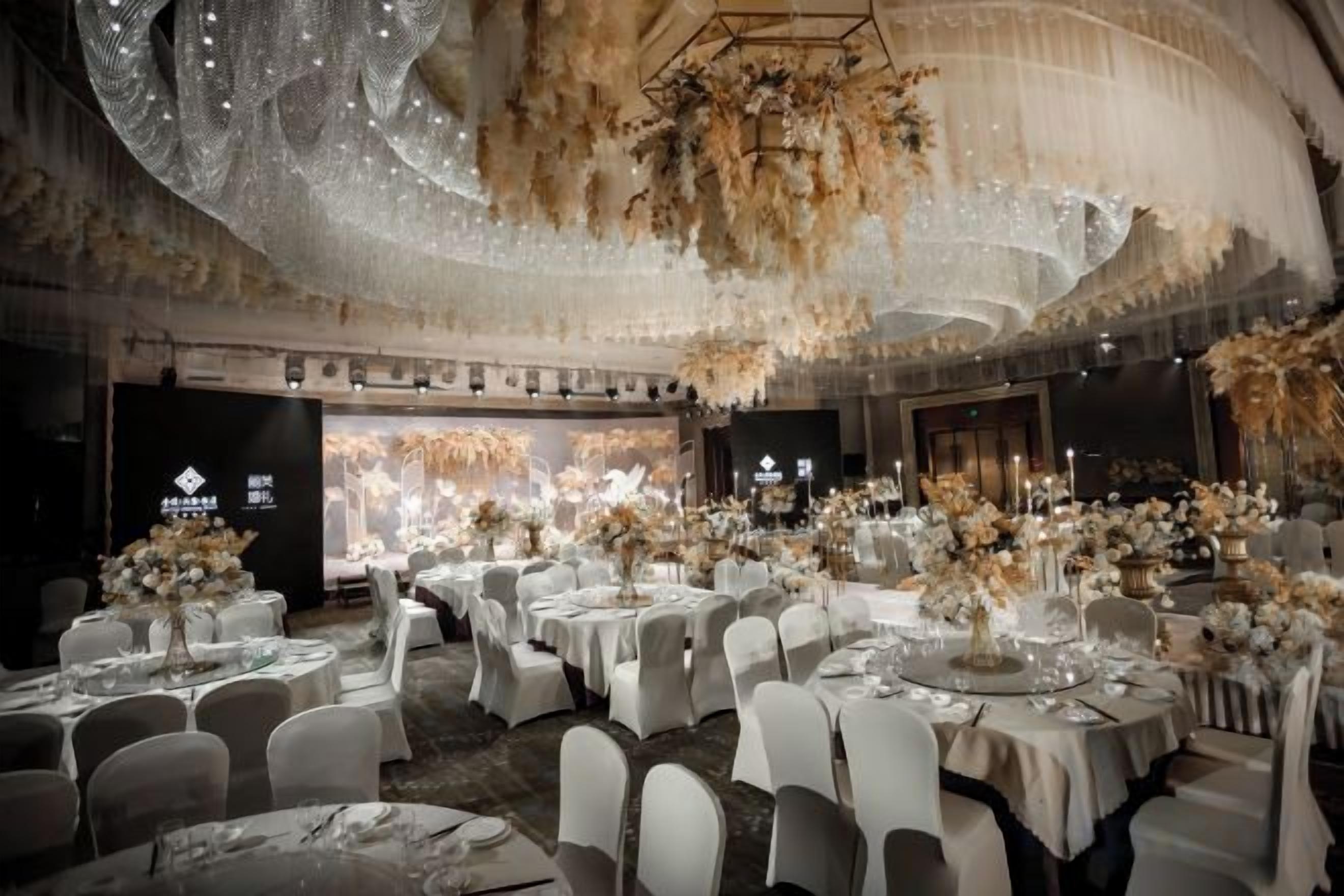 A banquet hall with round tables set for dining, a chandelier, and floral arrangements.