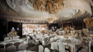 A banquet hall with round tables set for dining, a chandelier, and floral arrangements.