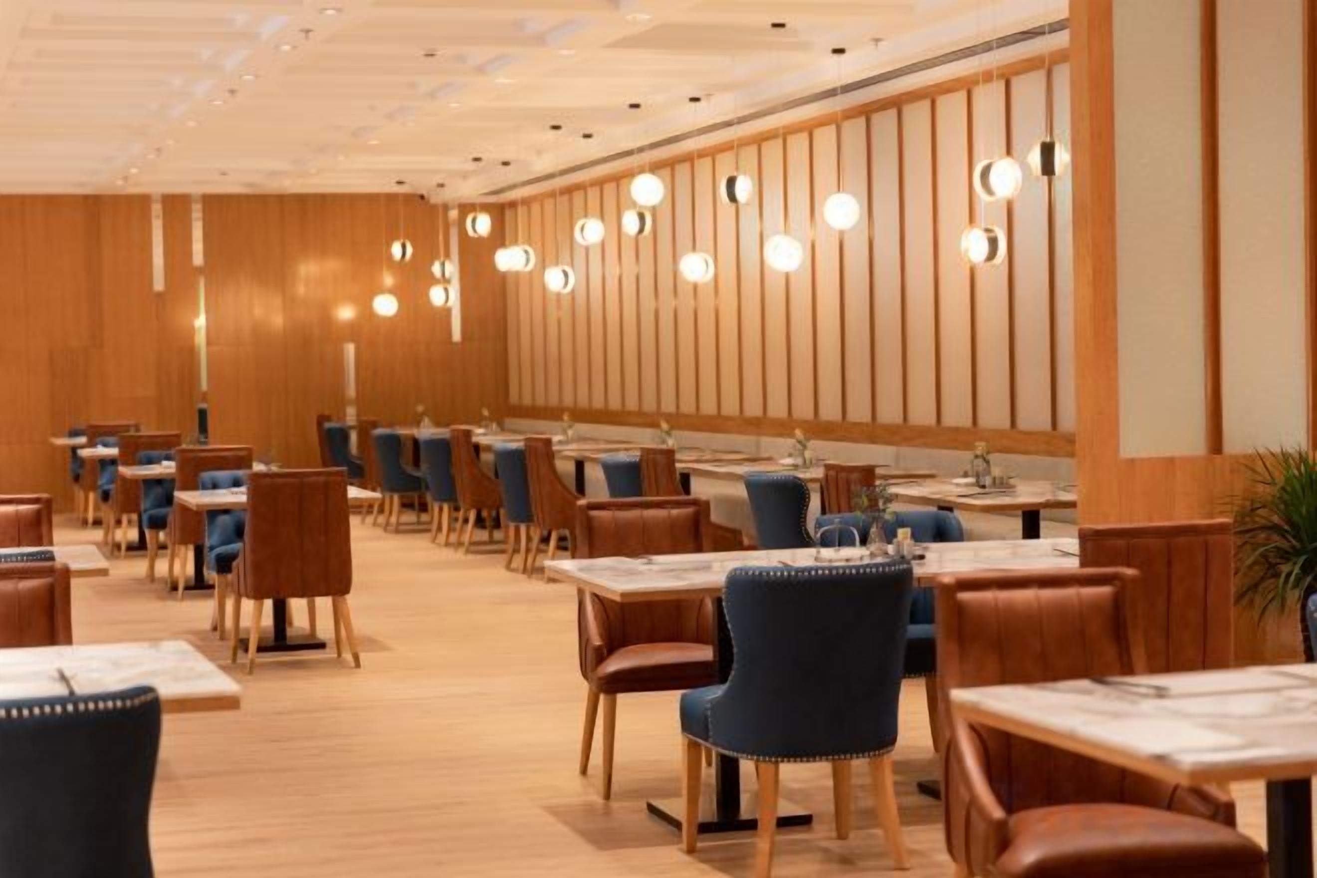 A restaurant with multiple tables and chairs, wooden panel walls, and hanging pendant lights.