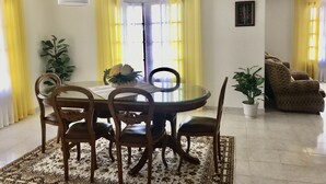 A dining area with a round table, chairs, and a vase of flowers. There are yellow curtains and a potted plant. - House with garden (Albufeira)