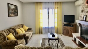 A living room with a sofa, armchairs, a coffee table, a TV, and a fireplace. - House with garden (Albufeira)
