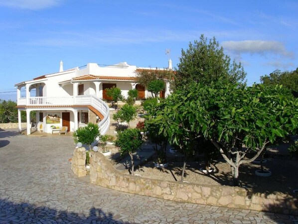 A two-story house with a balcony, a stone pathway, and a well-maintained garden with various plants.