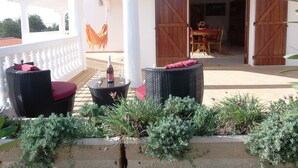 A covered outdoor seating area with wicker furniture and a table with a bottle and glasses. - House with garden (Albufeira)