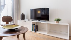 A modern living room with a flat-screen TV on a white entertainment unit, a round wooden table, and a bookshelf. - Puerta del Sol by Home at Homes (Sevilla)