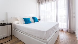 A modern hotel room with a large bed, a bedside table, and a window with sheer curtains. - Puerta del Sol by Home at Homes (Sevilla)