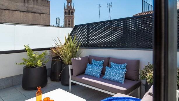 A rooftop terrace with a sofa, potted plants, and orange glasses on a table. - Puerta del Sol by Home at Homes (Sevilla)