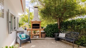 A patio with a brick-built outdoor oven, a bench, and a chair with a cushion.