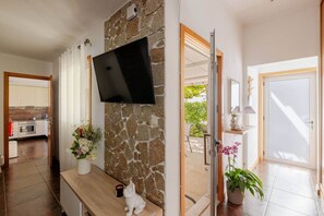 A modern kitchen with a stone wall, a flat-screen TV mounted above it, and a bench with a small dog figurine. - Casa do Fontanário (Penafiel)