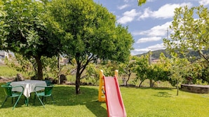 A grassy outdoor area with a picnic table and chairs, a red slide, and trees.