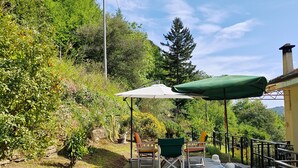 Une terrasse extérieure avec une table et des chaises, entourée d’une végétation luxuriante et d’arbres.