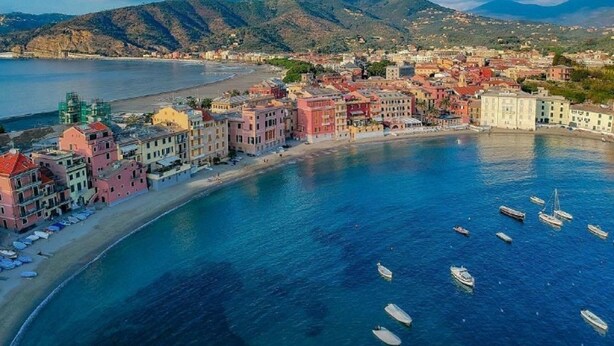 Une ville côtière aux bâtiments aux couleurs vives, avec une plage et des bateaux sur l’eau.