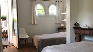 Una camera da letto con due letti singoli, pavimento in legno, una finestra con tende, un comodino con una lampada e un camino in mattoni.