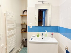 A bathroom with a white sink, blue-tiled walls, a mirror above the sink, and a radiator on the left.