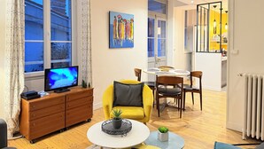 A modern living room with a TV, yellow sofa, dining table, and a view of the outside.