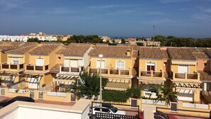 Una hilera de casas con techo de tejas de terracota y balcones, cielo despejado y una vista distante del mar.