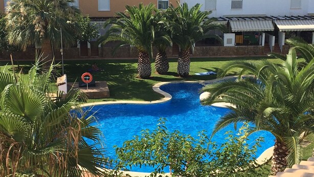 Una piscina rodeada de palmeras y un edificio con techo de tejas.