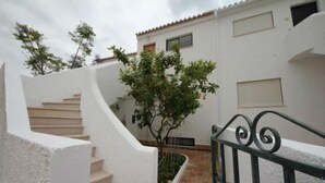 A white building with a staircase leading to a door, a tree in the foreground, and a metal railing.