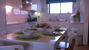 A modern kitchen with white cabinets, a dining table set with bowls and plates, and a window with blinds.