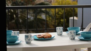 A balcony with a table set for tea, including blue cups and saucers, and a plate of pastries.