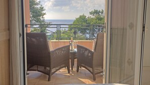 A balcony with wicker chairs and a small table, overlooking a scenic view of the sea and trees. - 4 bed sleeps 8  beach front villa with Shared Pool and Private Garden. (Roquebrune-Sur-Argens)