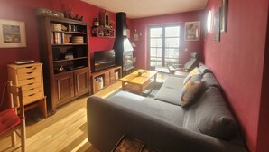 A living room with a sofa, wooden cabinet, television, and a fireplace. - Magic Pirineos, Apartment in Linsoles, Valle de Benasque with Pool and WIFI  (Anciles)