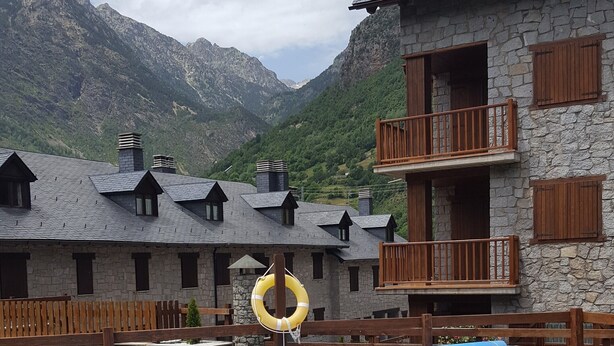 A swimming pool with a lifebuoy, surrounded by stone buildings with wooden balconies, set against a mountainous backdrop. - Magic Pirineos, Apartment in Linsoles, Valle de Benasque with Pool and WIFI  (Anciles)