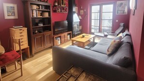A living room with a sofa, wooden coffee table, and a TV. There is a bookshelf and a window with curtains. - Magic Pirineos, Apartment in Linsoles, Valle de Benasque with Pool and WIFI  (Anciles)