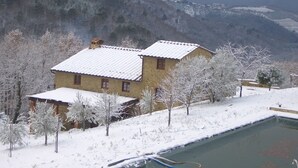 A stone building with a snow-covered roof, surrounded by snow-laden trees and a view of distant mountains. - Villa on Chianti hill in heart of Tuscany, super-large pool, 14 ha plot (Gaiole in Chianti, Prov. Siena, Toscana)