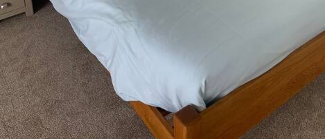 A neatly made bed with a wooden headboard, a bedside table with a lamp, and a wooden dresser.