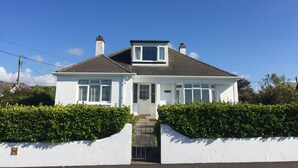 A two-story house with a white exterior, a front door, and a small front porch. - Hill Rise Cottage in beautiful Trevone Bay, near Padstow, North Cornwall (Trevone, Padstow)