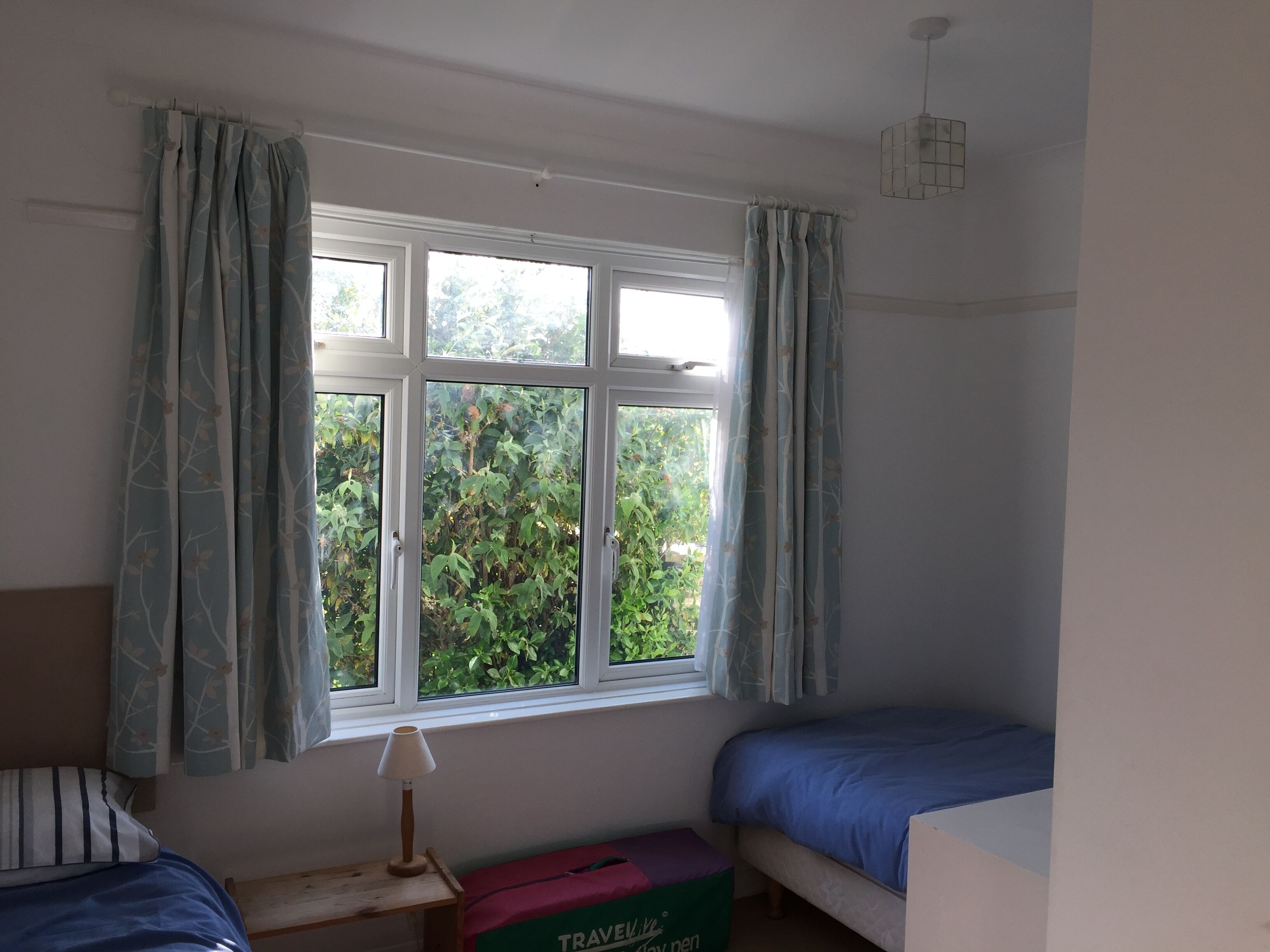 Une chambre avec une fenêtre, une table de chevet avec une lampe, un lit et une valise.