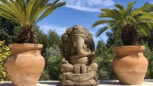 Una scultura in pietra raffigurante un elefante, in un giardino con due grandi vasi in terracotta ai lati.