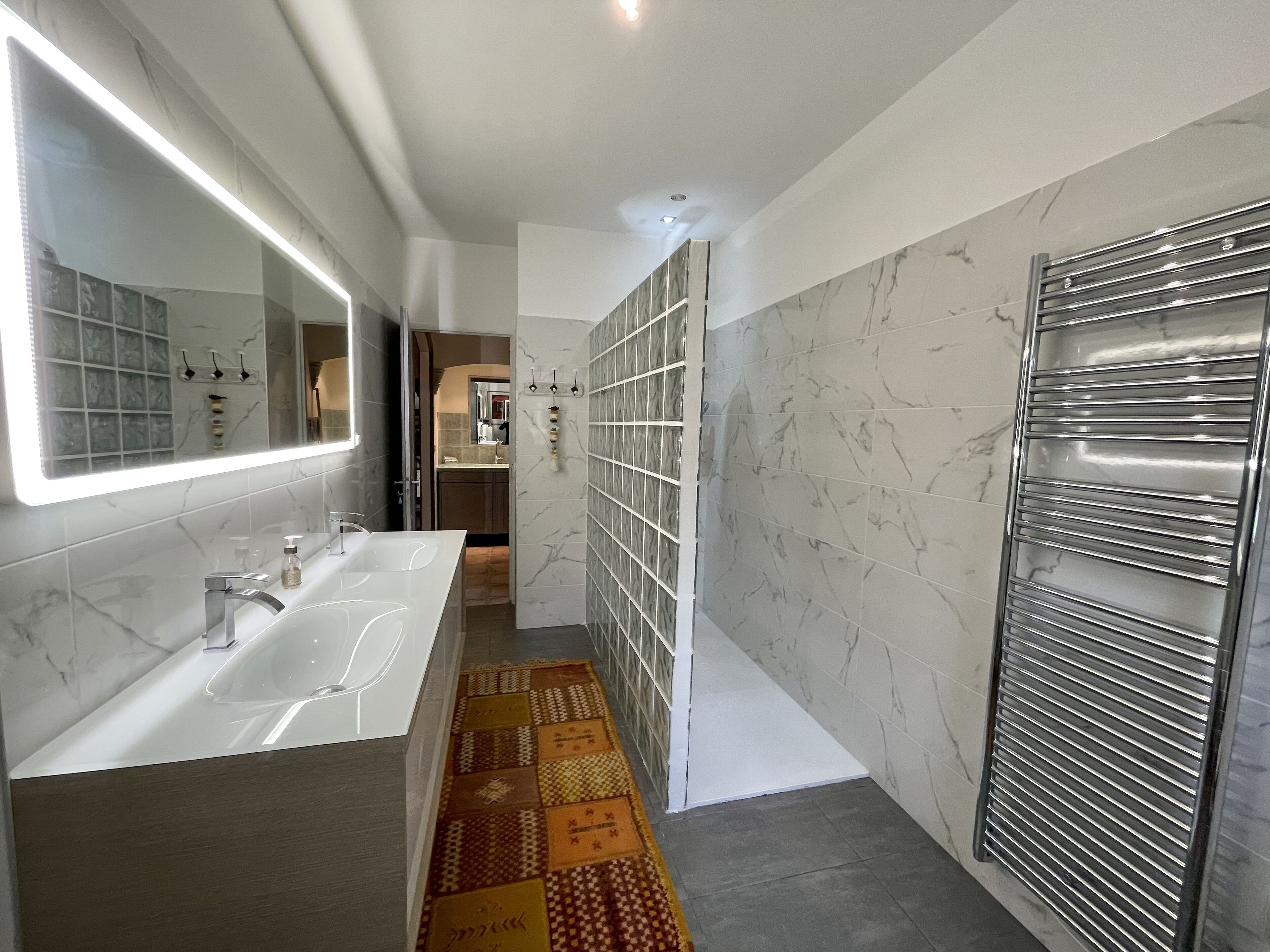 A modern bathroom with a large mirror, white marble tiles, and a shower with a glass door.