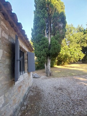 A rustic stone building with a window and shutters, a tree in the foreground, and a grassy area with a gravel path. - Shed the heart of Provence (Saint-Rémy-De-Provence)