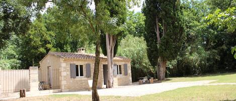 A stone house with a tiled roof, surrounded by trees and a grassy yard.