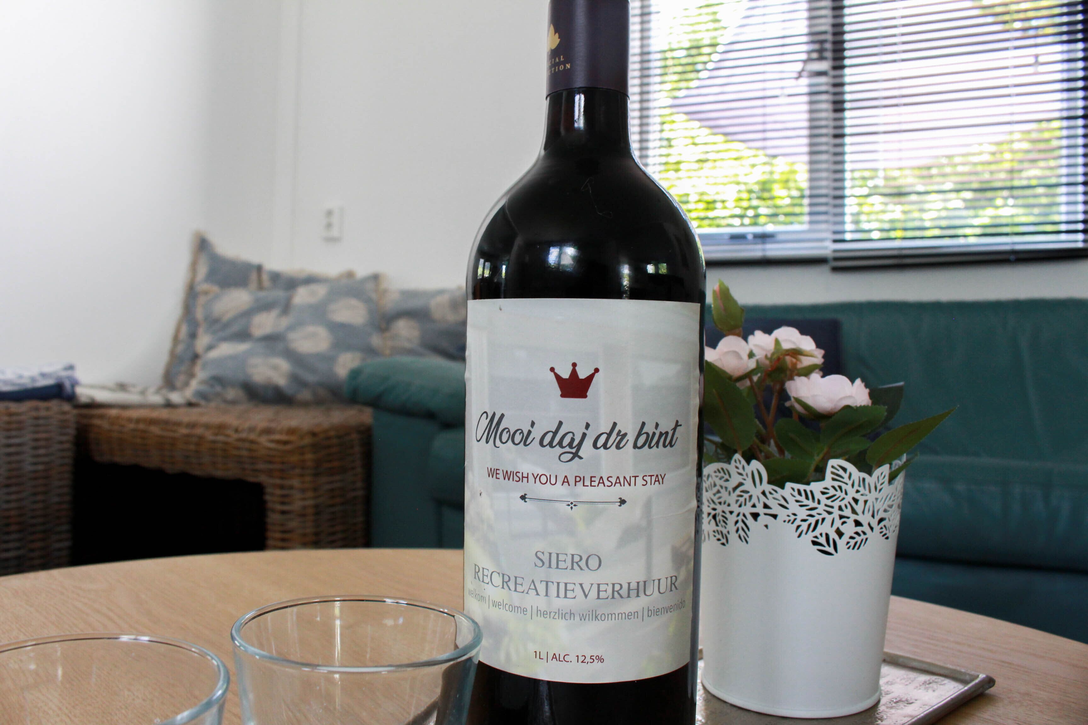 Una bottiglia di vino con etichetta, due bicchieri e un vaso decorativo su un tavolo.