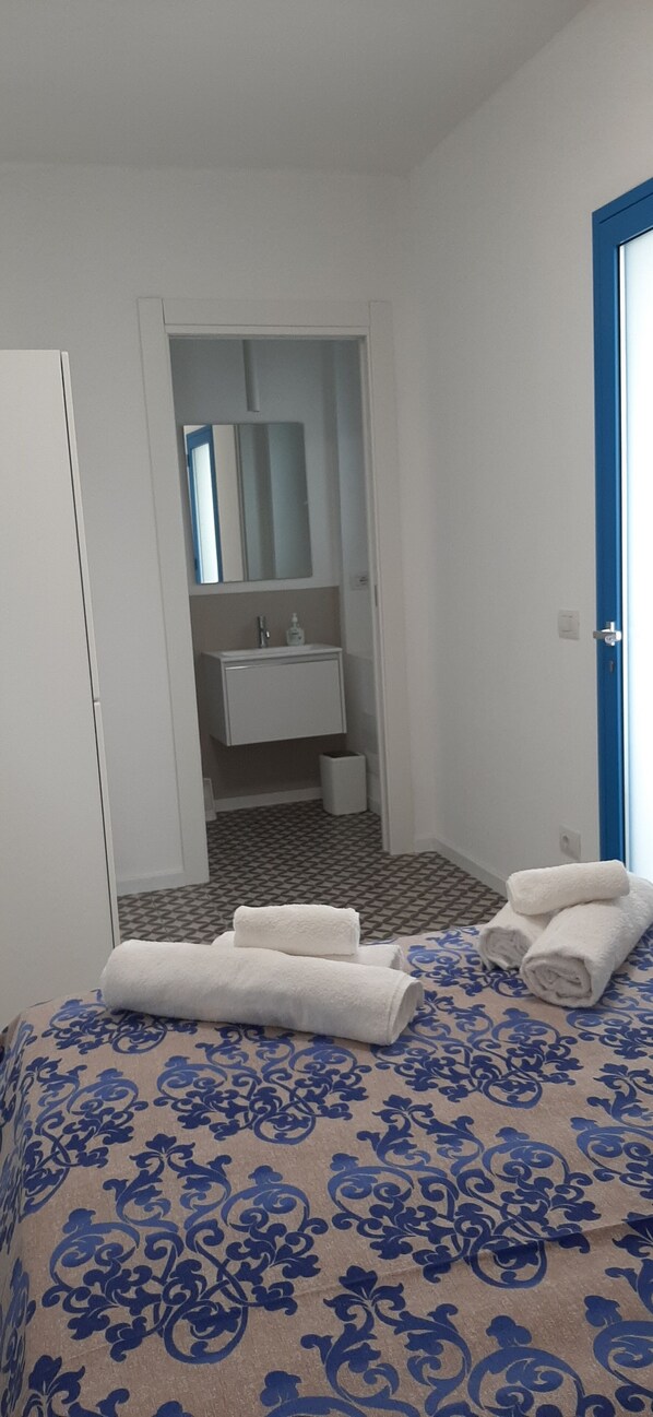 A hotel room with a bed, a bathroom with a mirror and sink, and a blue door.