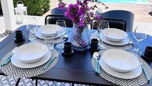 A table set for four with white plates, black cutlery, and a vase of purple flowers, overlooking a pool and ocean. - Holiday Home Sciacca (San Giorgio)