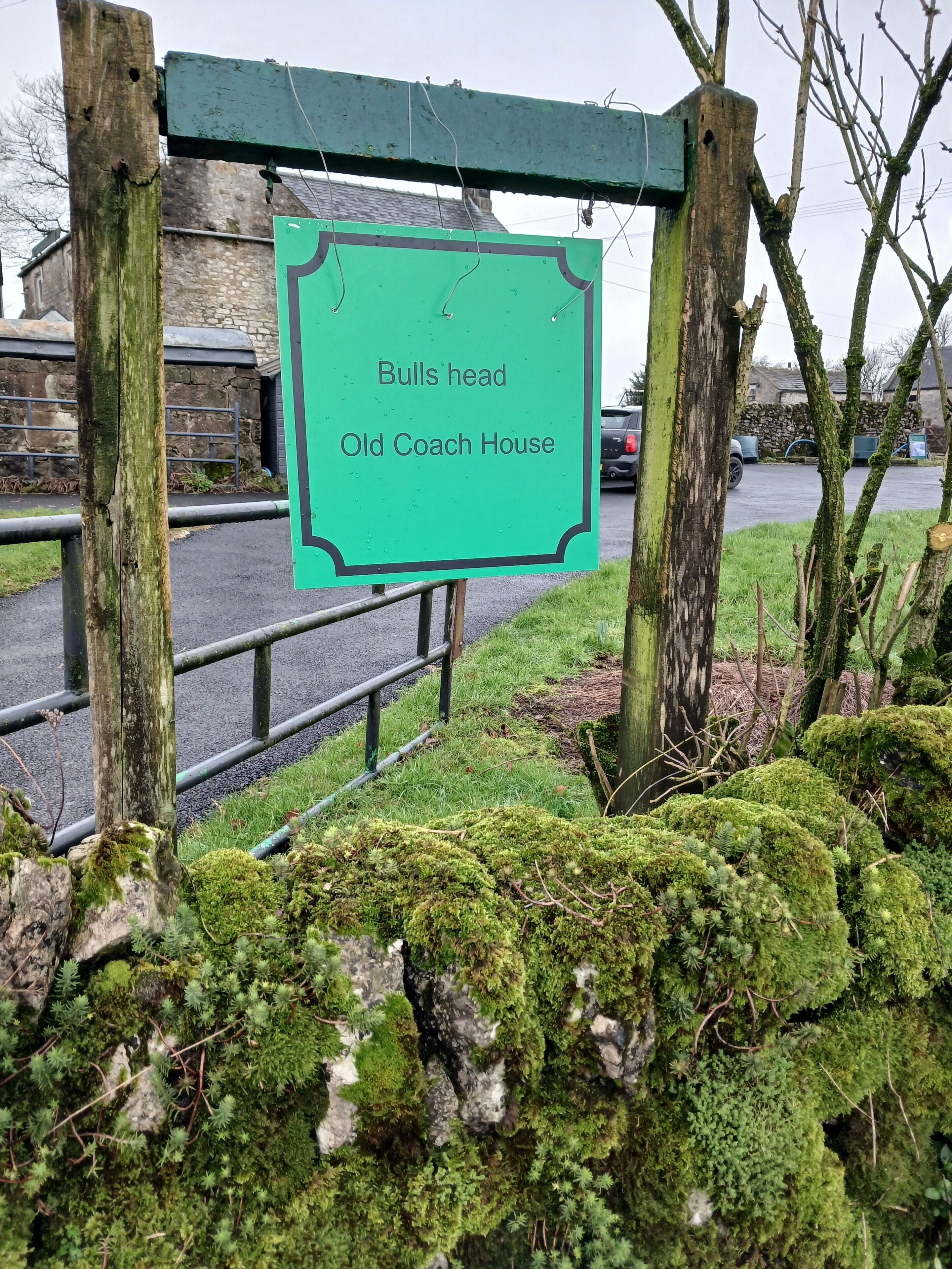 A sign for 'Bulls Head Old Coach House' with a rustic wooden post and a green background.