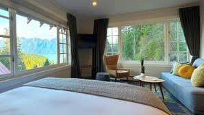 A hotel room with a large bed, a sofa with patterned cushions, a small table, a chair, and a TV. - Artisan Suites on Bowen (Bowen Island)