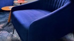 A room with a large window, two blue armchairs, a small round table with a teapot, and a view of trees and a building outside. - Artisan Suites on Bowen (Bowen Island)