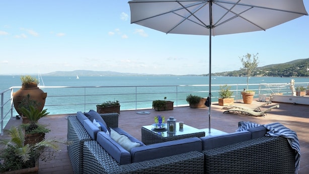 A terrace with wicker furniture, a large umbrella, and potted plants. - The villa is located above the sea, direct sea access with a wonderful view (Porto Santo Stefano)