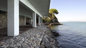 A coastal building with a stone pathway leading to a rocky shoreline. - The villa is located above the sea, direct sea access with a wonderful view (Porto Santo Stefano)