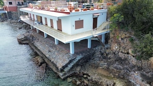 A waterfront building with a balcony, a staircase leading to the upper level, and a rocky shoreline. - The villa is located above the sea, direct sea access with a wonderful view (Porto Santo Stefano)