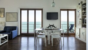 A spacious living area with a dining table, white chairs, a blue sofa, and a TV mounted on the wall. - The villa is located above the sea, direct sea access with a wonderful view (Porto Santo Stefano)