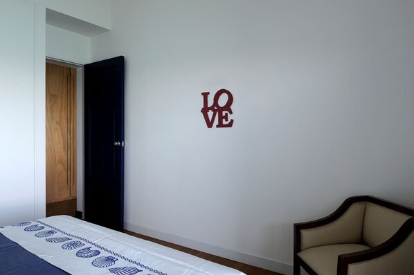 Ein Schlafzimmer mit Bett, Sessel, Kleiderschrank und Wand mit 'LOVE'-Dekoration.