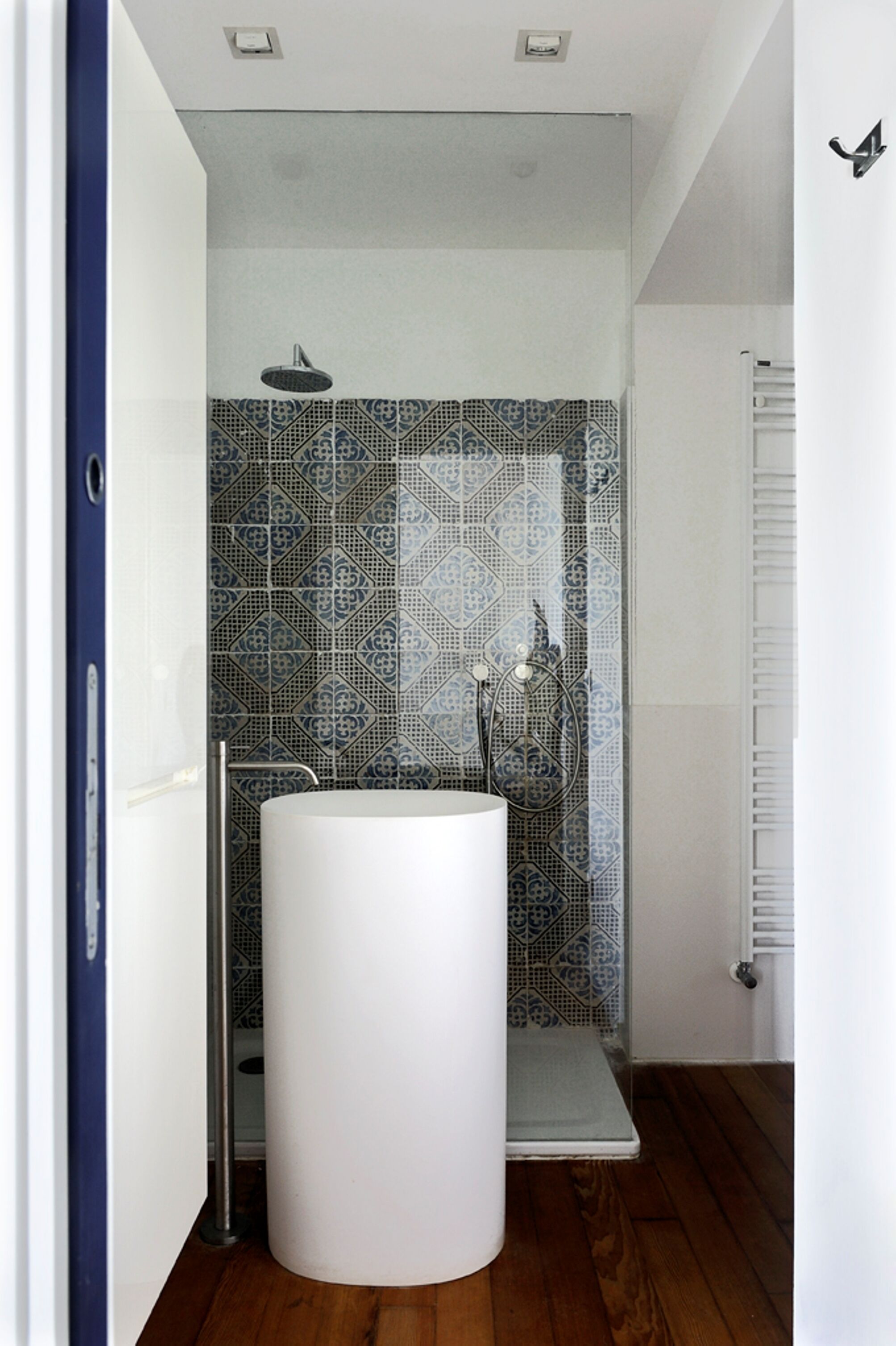 A bathroom with a white sink, patterned shower wall, and wooden flooring.