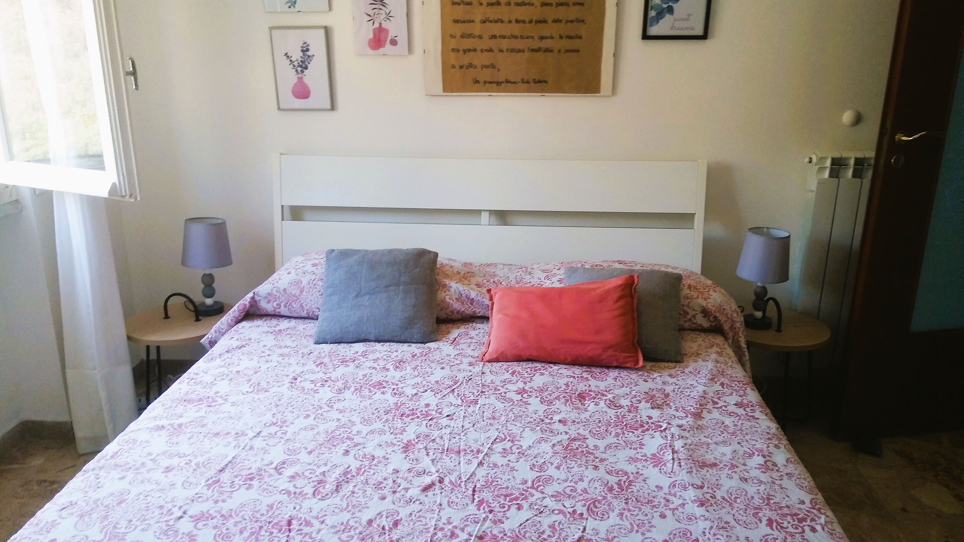 A bed with a patterned bedspread, two pillows, and a white headboard. There are two bedside tables with lamps.